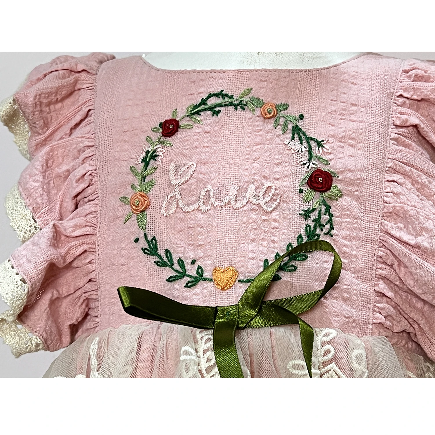 Pink dress with flutter sleeves and trimed with eyelet lace, has hand embroidery in the chest