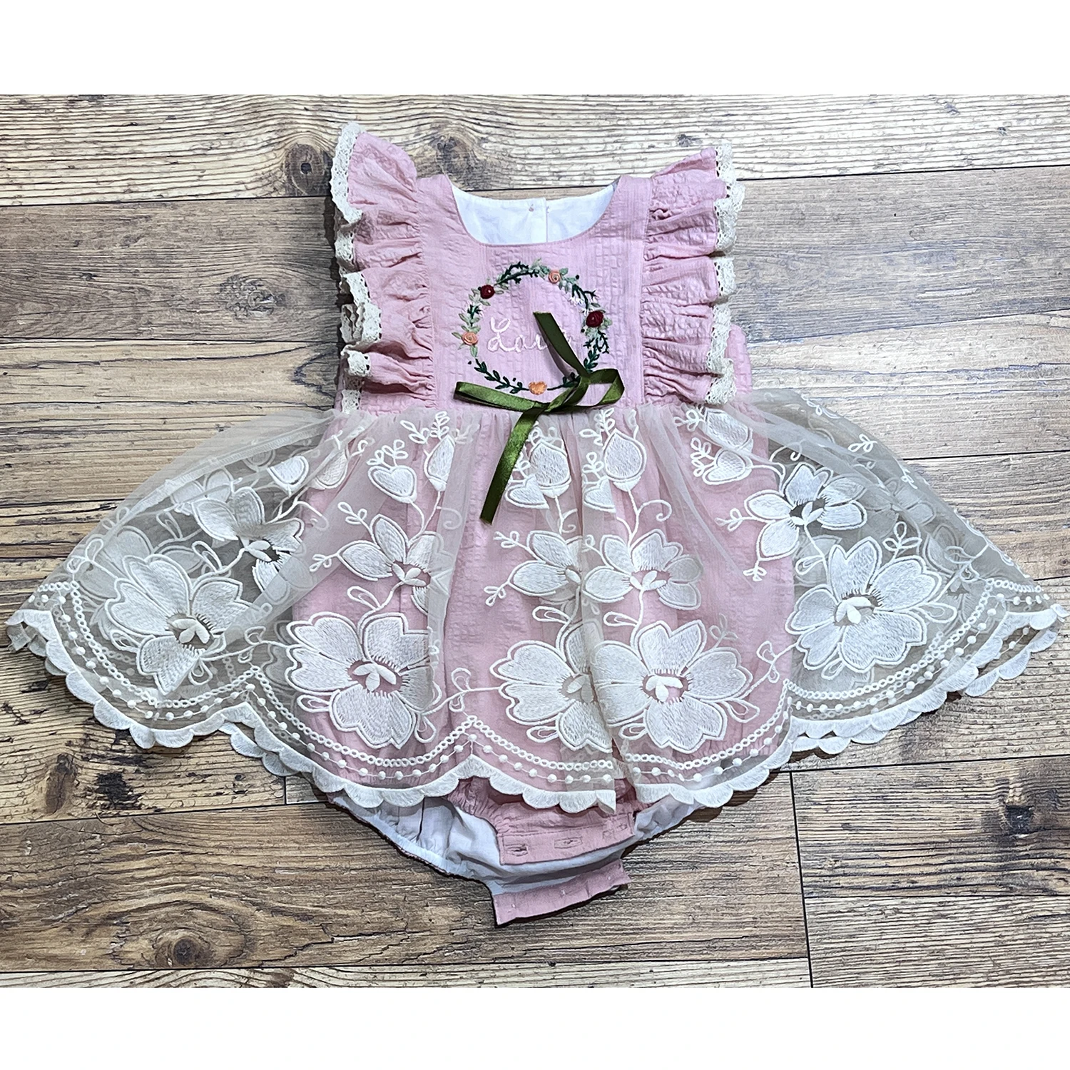 Pink dress with flutter sleeves and trimed with eyelet lace, has hand embroidery in the chest