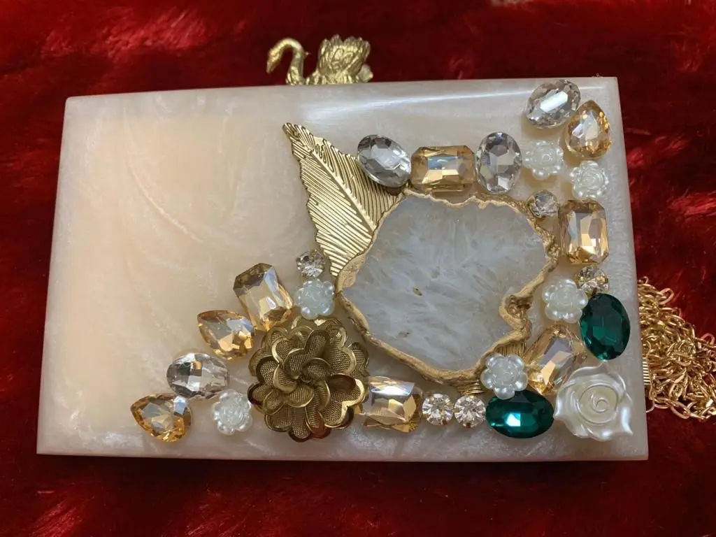 Featuring clutch in mother of pearl base with embedded rhinestones It has a gold chain sling, a magnetic closure.