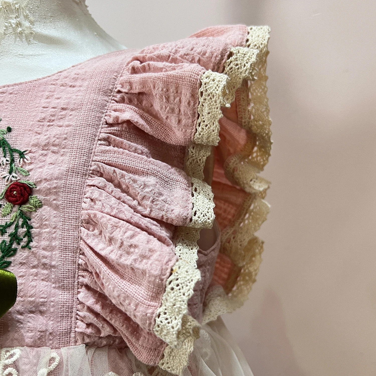 Pink dress with flutter sleeves and trimed with eyelet lace, has hand embroidery in the chest
