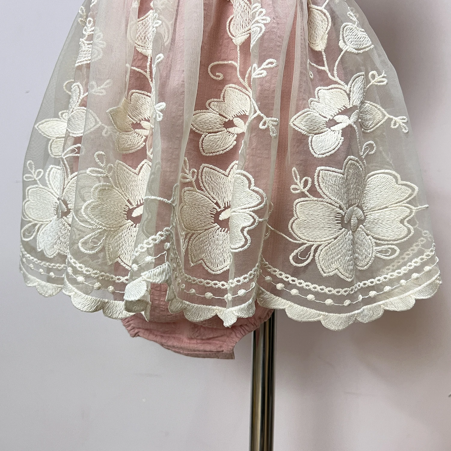 Pink dress with flutter sleeves and trimed with eyelet lace, has hand embroidery in the chest