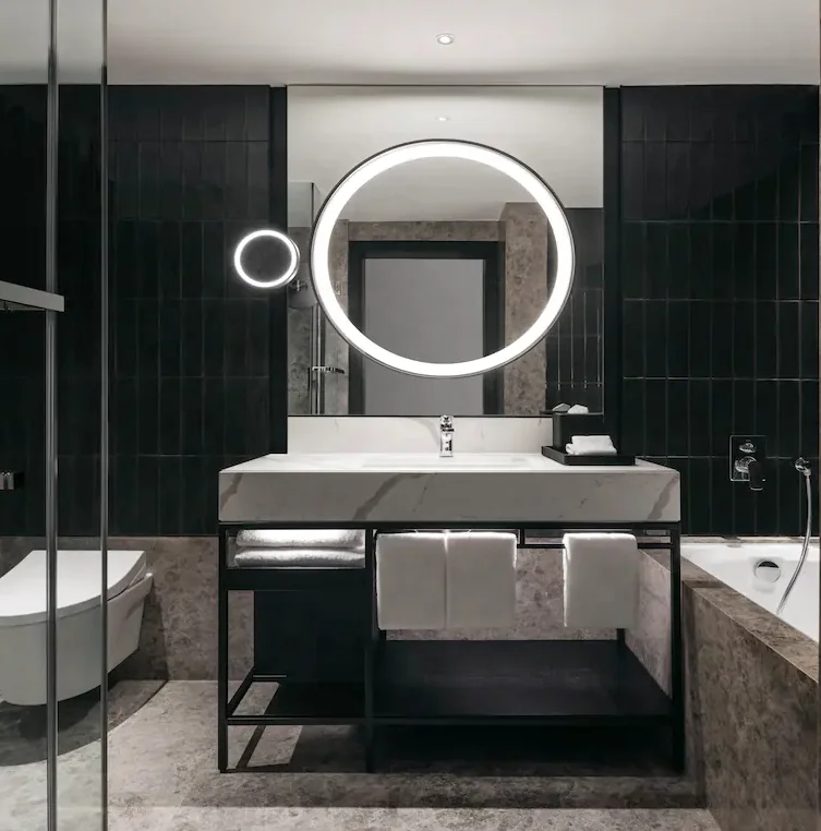 Double wood vanity include matte black faucets and oval mirrors soft blue tile and freestanding bath welcomes relaxation